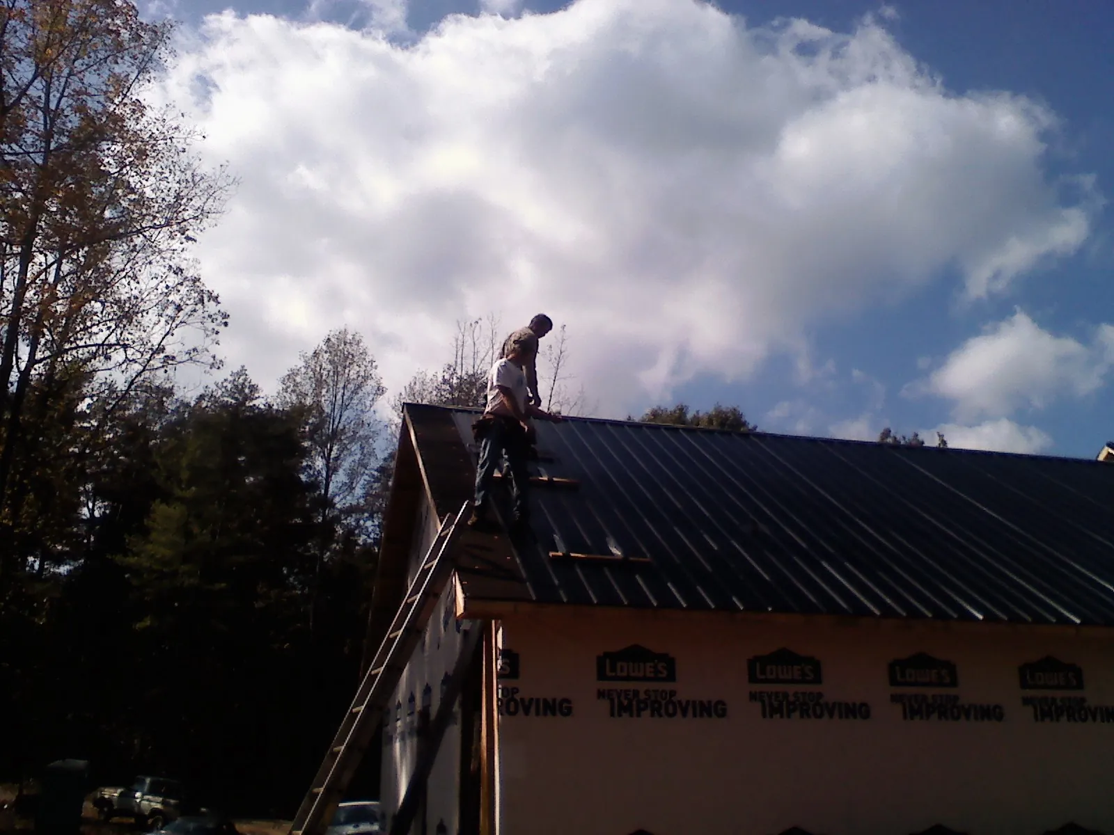 Roofer fastening dark metal panels high against a cloudy sky, from a Roof Inspection job in Manassas