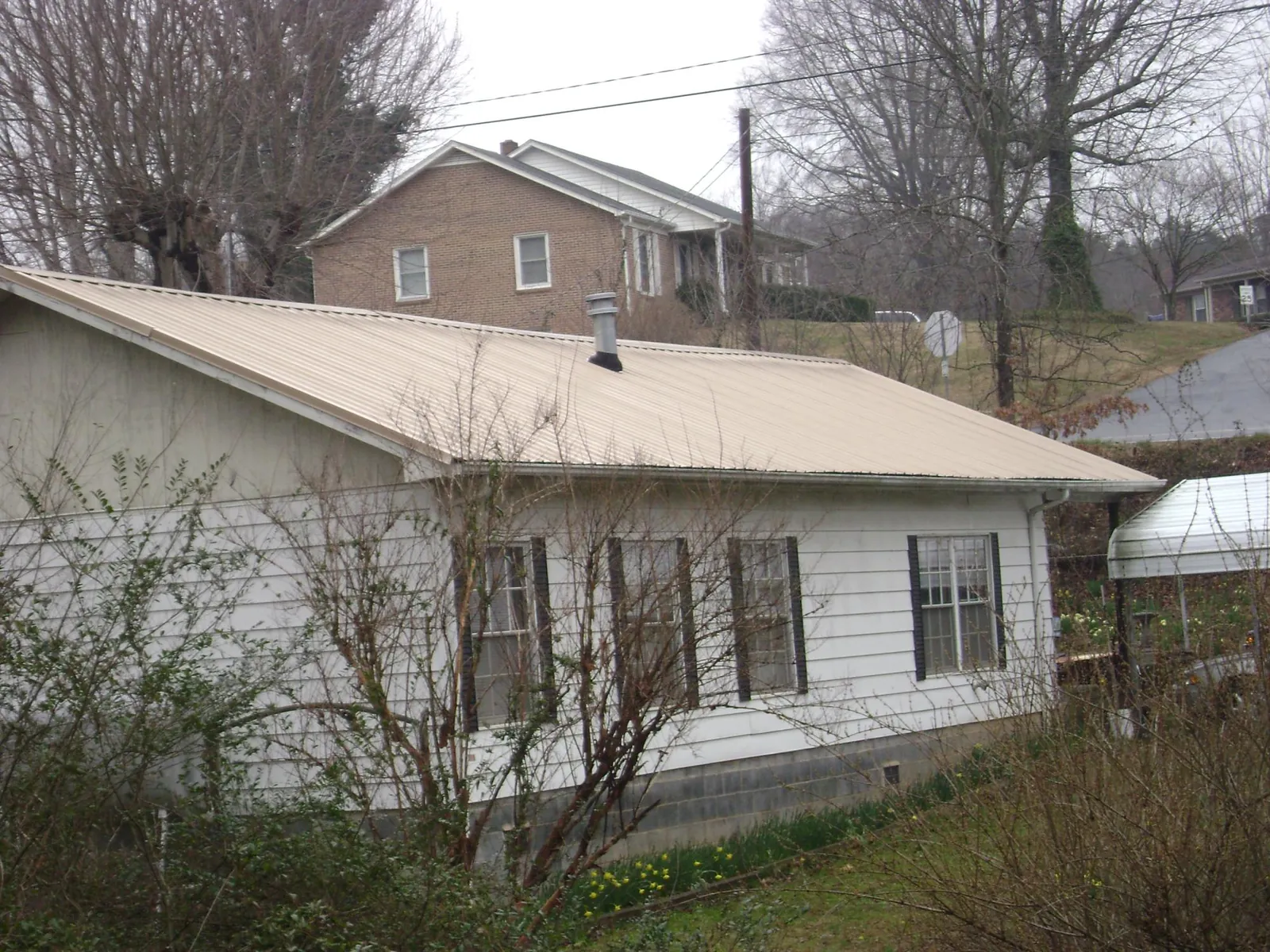 Tan metal roof on a white sided house set into a hillside — Commercial Roofing by Roofing Brothers in Manassas